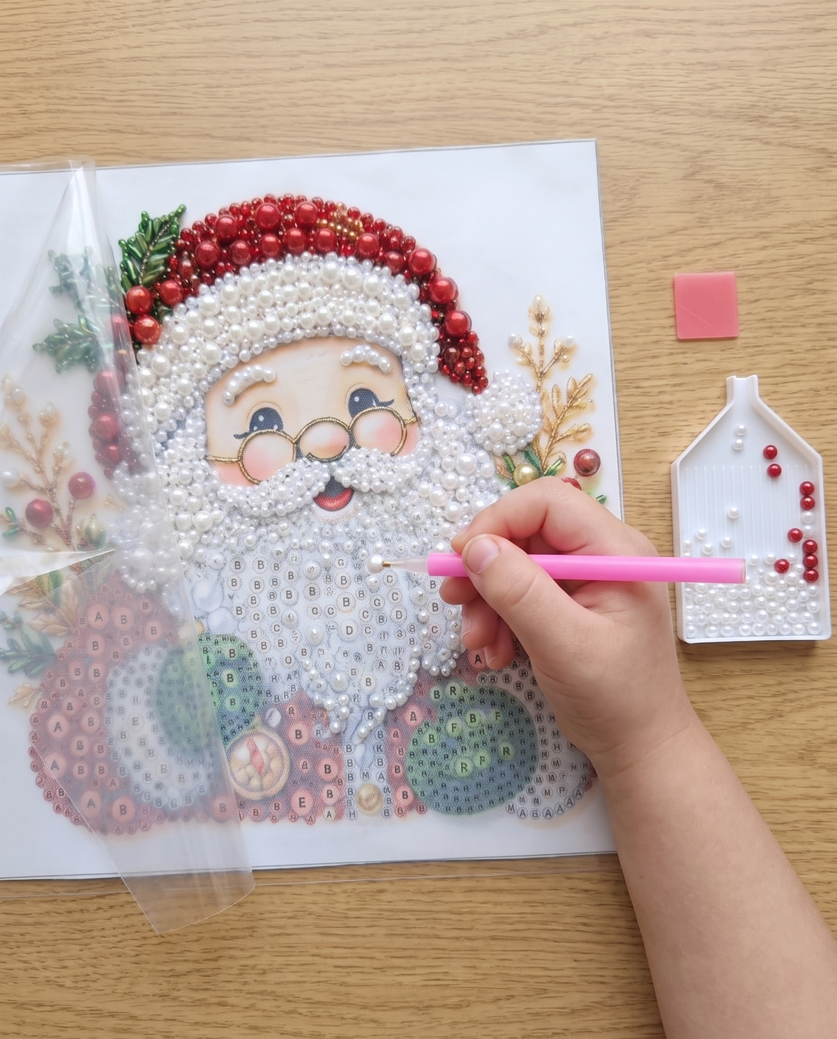 Main d'enfant qui pose une perle avec le stylo sur la toile Père Noël